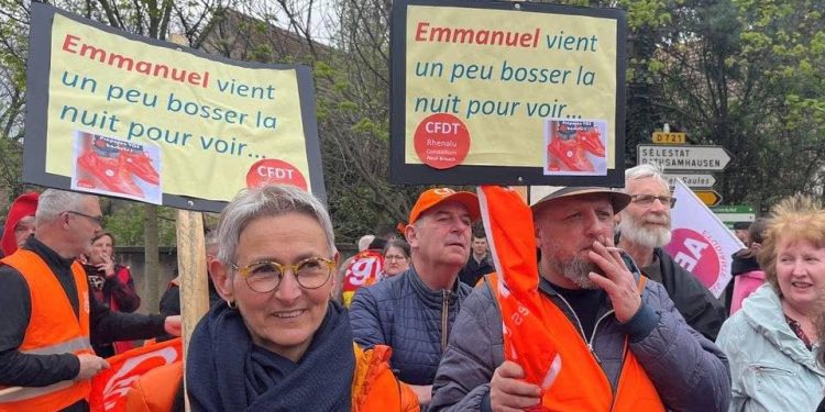 Protesters, wearing CFDT labour union vests, attend a demonstration against pension law before the arrival of French President Emmanuel Macron in Muttersholtz, Eastern France, April 19, 2023.The slogan reads "Emmanuel, come and work a little at night to see". REUTERS